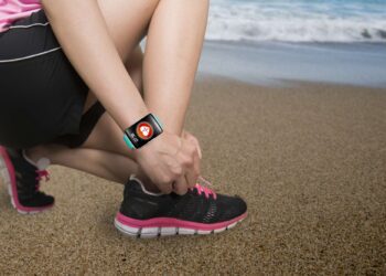Sport woman hand tying shoelaces wearing touchscreen smartwatch with health sensor app icon on natural sea beach background.